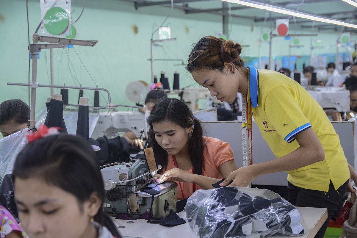 Kaksi naista kumartuneena ompelukoneen ääreen myanmarilaisessa vaatetehtaassa