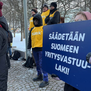 Ihmisiä mielenosoituksessa EU:n yritysvastuudirektiivin ja Suomen yritysvastuulain puolesta. Kyltissä lukee: Säädetään Suomeen yritysvastuulaki.