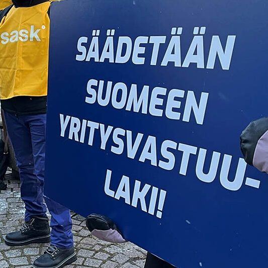 Ihmisiä mielenosoituksessa EU:n yritysvastuudirektiivin ja Suomen yritysvastuulain puolesta. Kyltissä lukee: Säädetään Suomeen yritysvastuulaki.